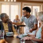 Happy senior people and caregiver talk in dining room at nursing home.