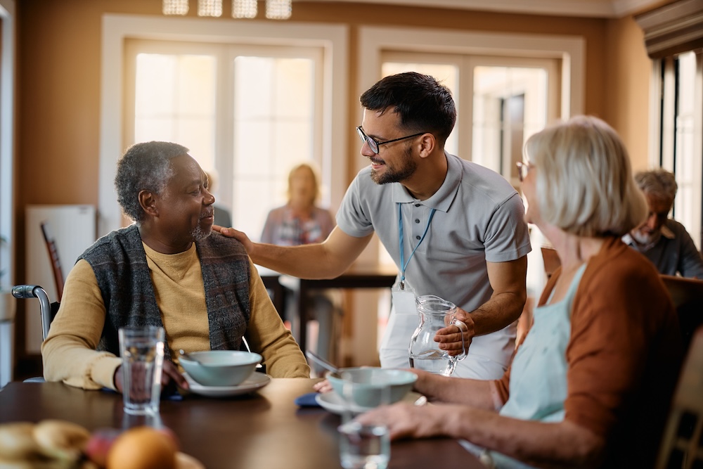 Happy senior people and caregiver talk in dining room at nursing home.